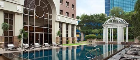 A swimming pool with lounge chairs and a gazebo in a hotel courtyard.
