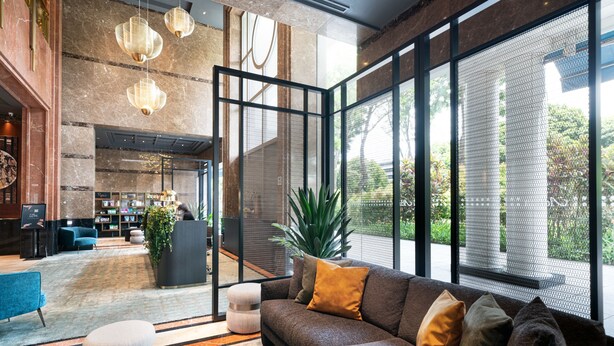 Eine moderne Lobby mit einem Ecksofa, einem runden Couchtisch und einem großen Fenster mit Blick auf Grünflächen.