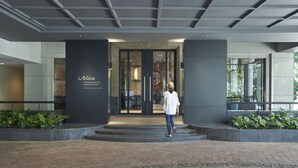 Ein moderner Eingangsbereich mit Glastür, eine Person geht darauf zu, und ein Schild mit der Aufschrift 'Adina serviced environment Singapore Orchard'.