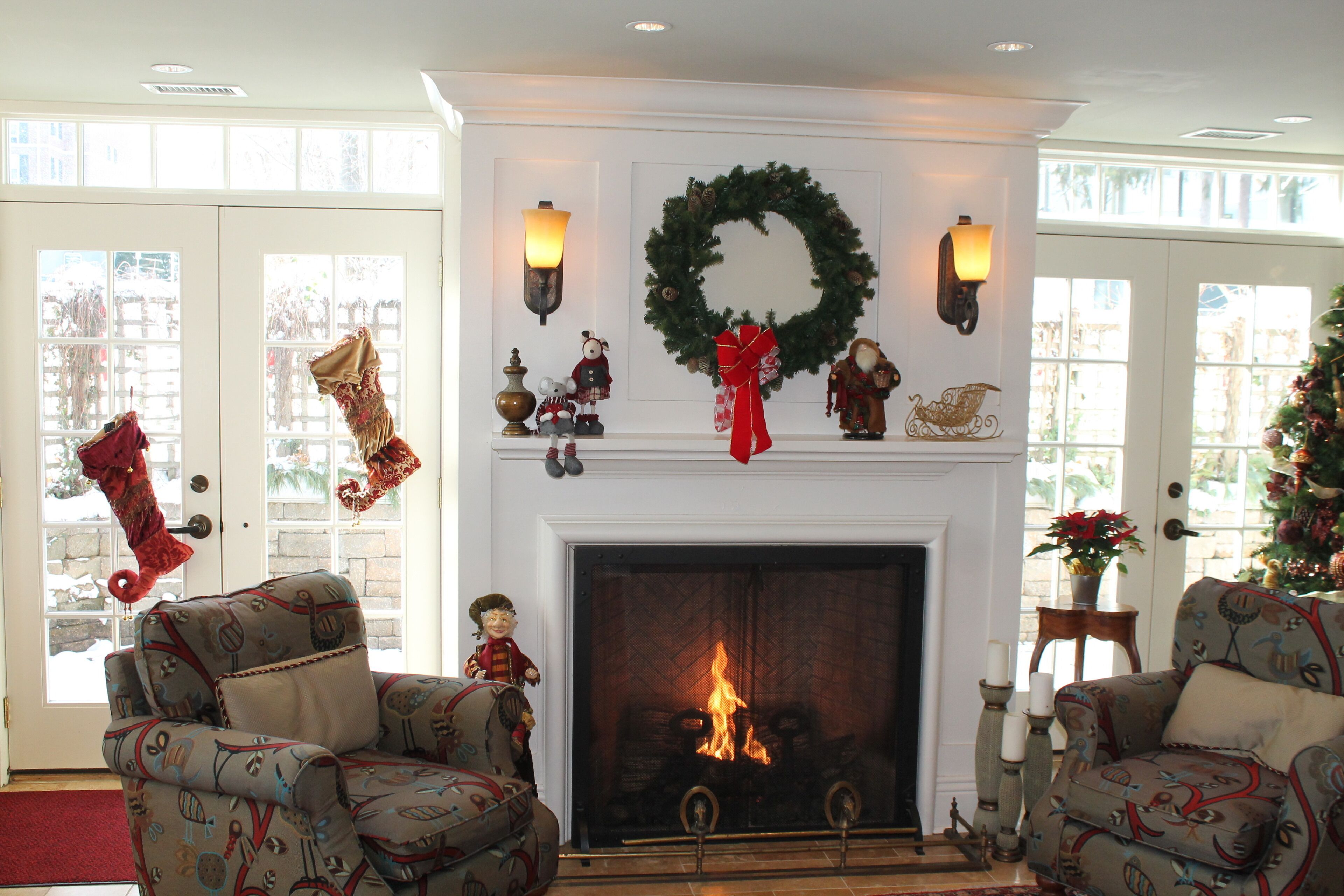 A cozy living room with a fireplace, two armchairs, and a Christmas wreath above it.