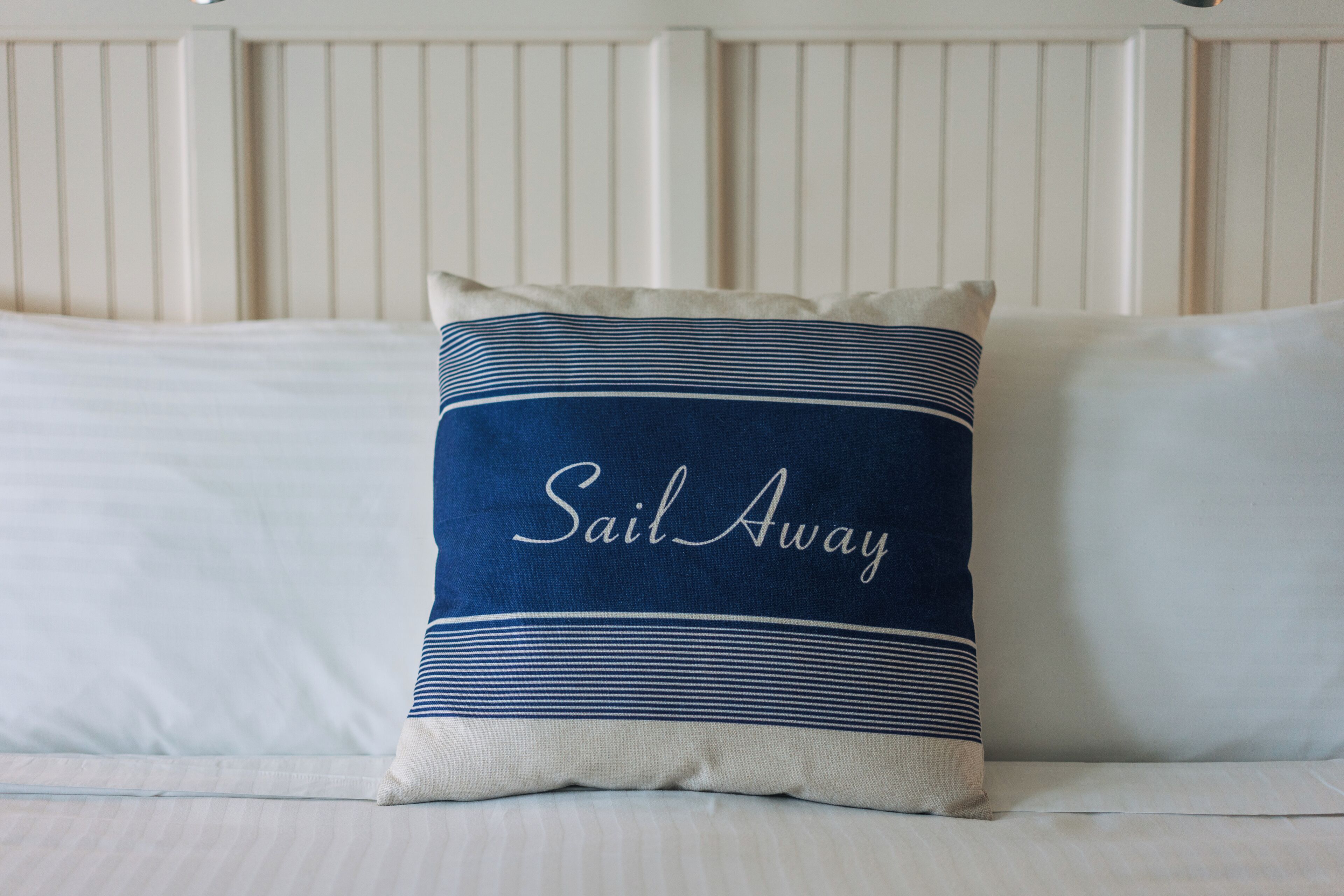 A bed with a pillow featuring the text "Sail Away" and a striped design.