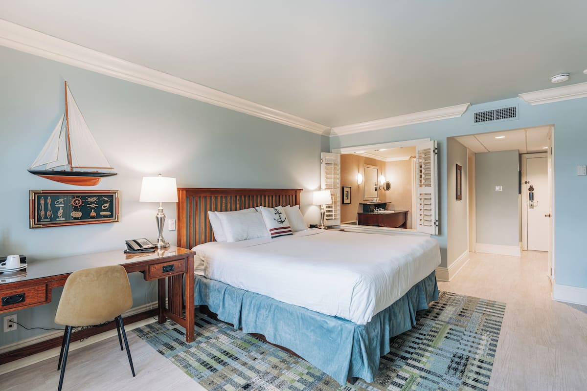 A hotel room with a large bed, a desk with a chair, a lamp, and a framed picture on the wall.