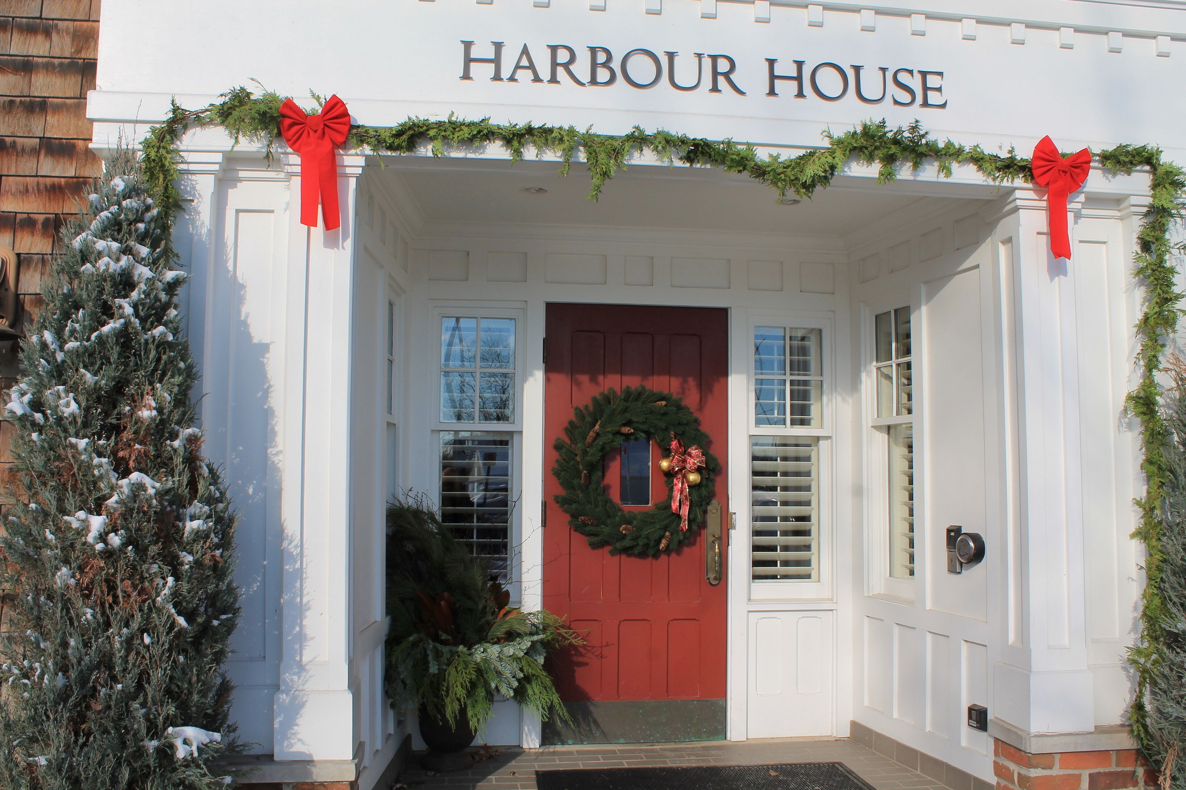Un edificio con una puerta roja, identificado con la placa “Harbour House”, decorado con una corona y guirnaldas.
