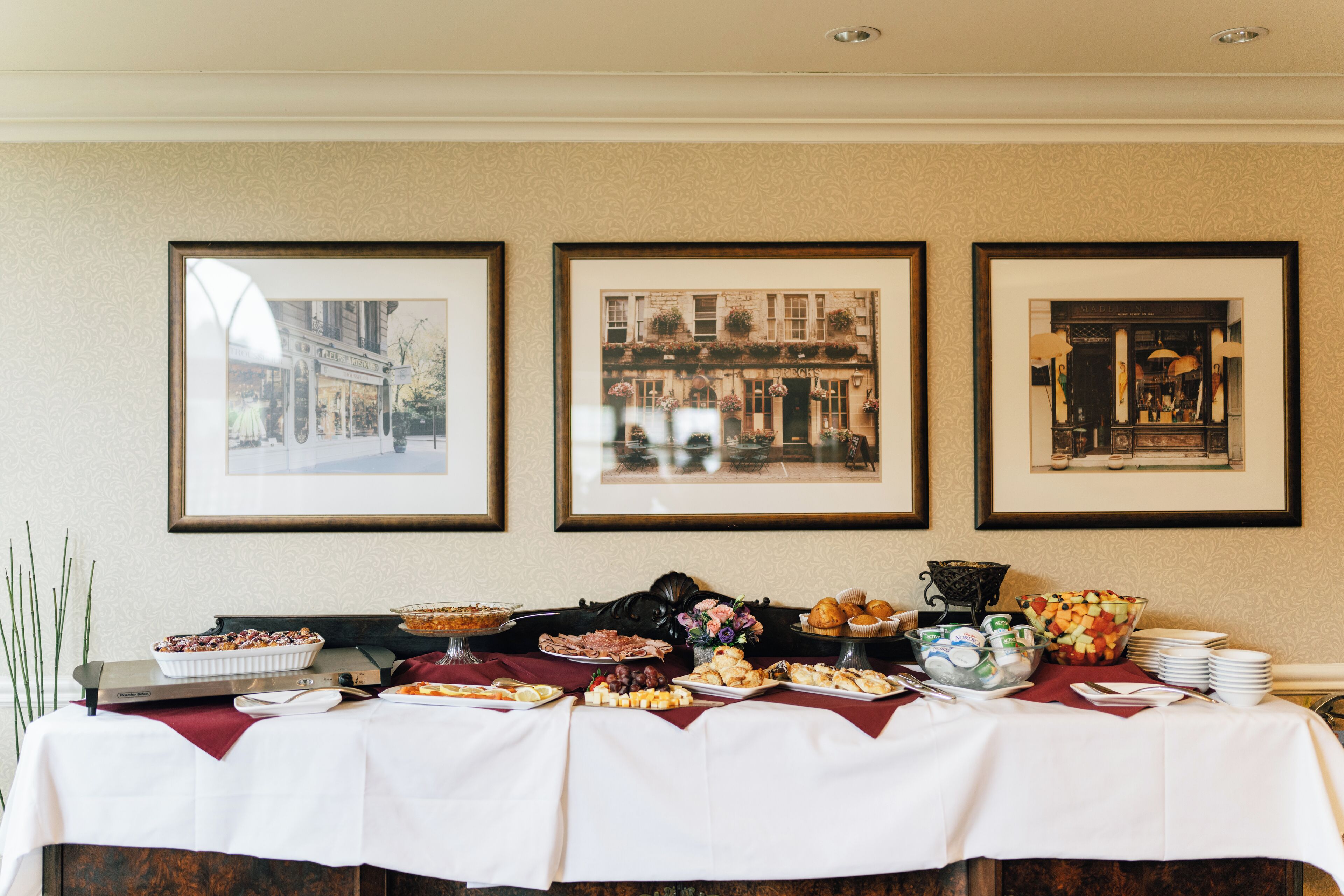 A buffet table with various food items and framed pictures on the wall behind it.
