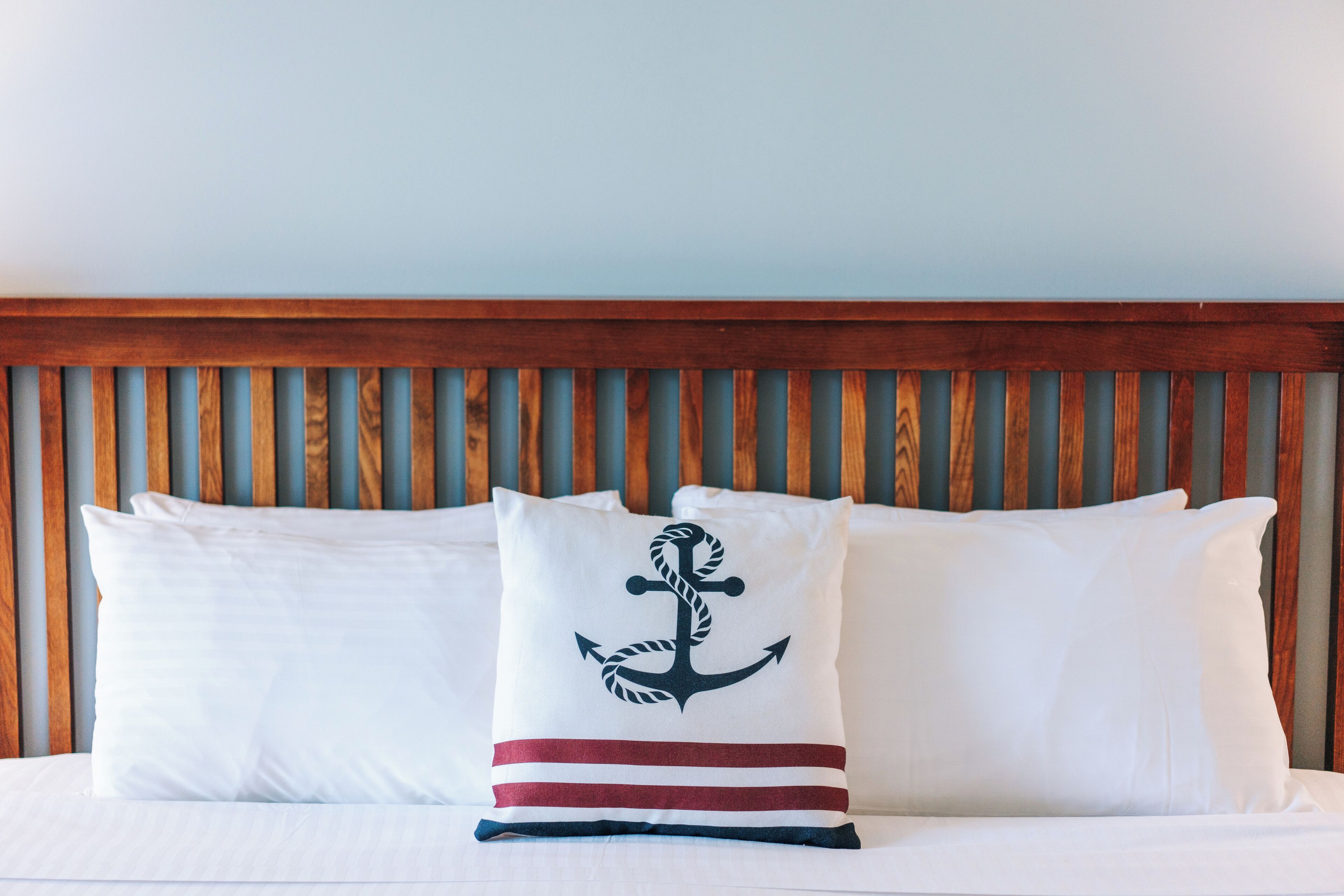 A bed with white bedding and pillows, one with a nautical anchor design.