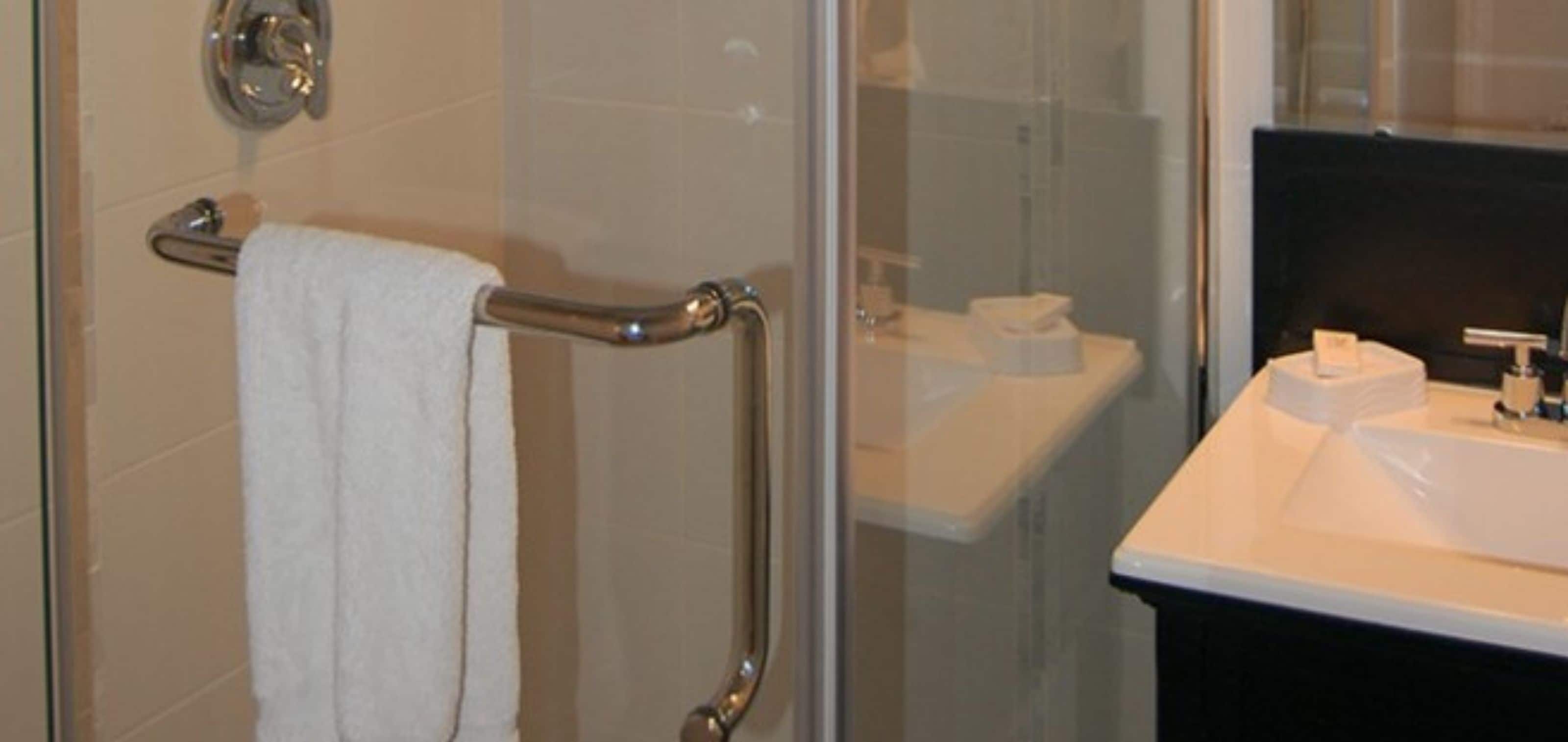 A bathroom with a glass shower enclosure, a white sink, and a towel rack.