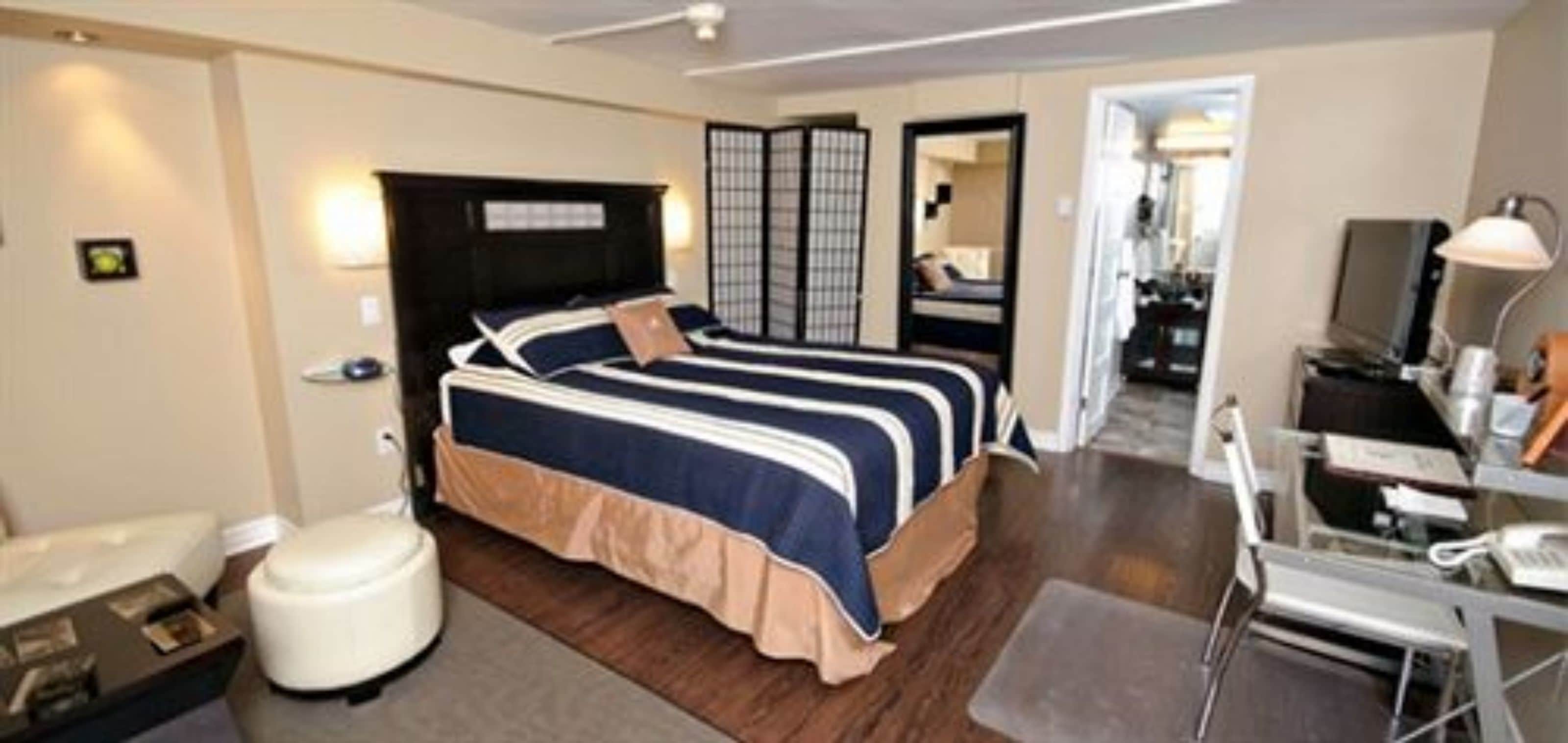 Una habitación de hotel con cama, escritorio, silla, espejo y armario.