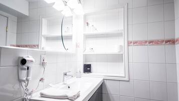 Casa de banho com lavatório branco, secador de cabelo e estantes com produtos de higiene pessoal.