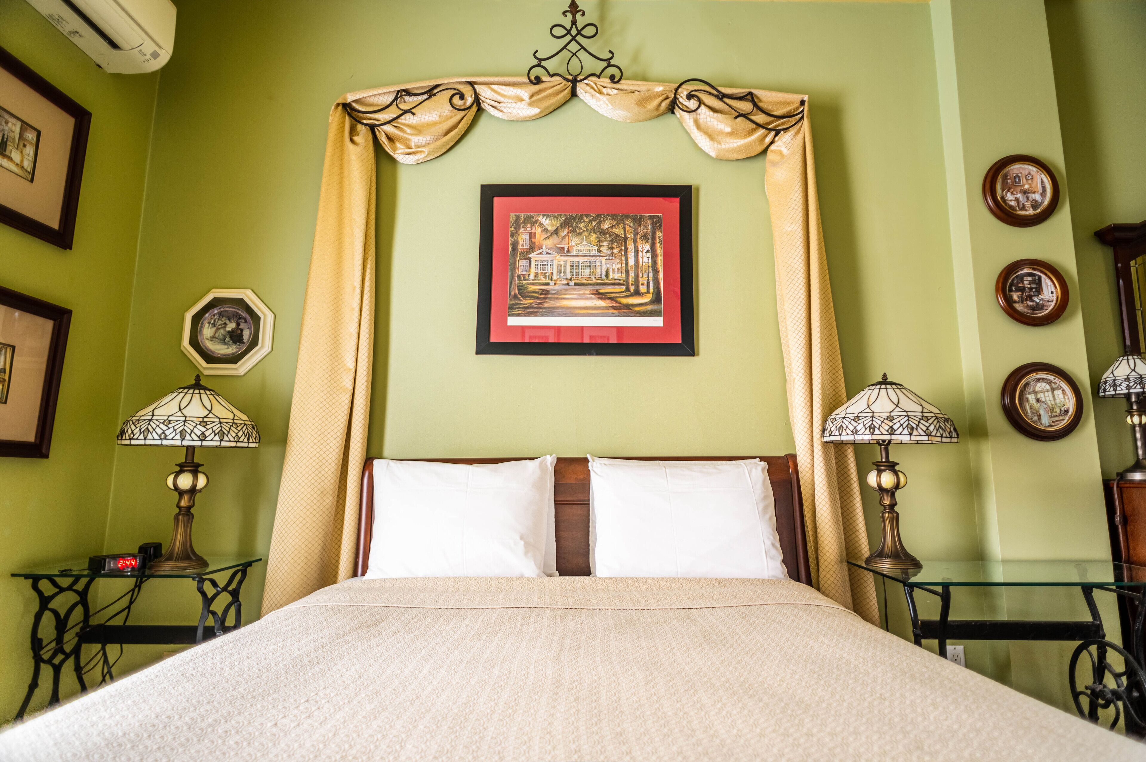 A neatly made bed with a canopy, framed artwork on the wall, and two bedside lamps.