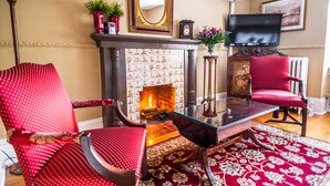 Una sala de estar con chimenea, dos sillones tapizados en rojo, una mesa de centro de vidrio y un televisor.