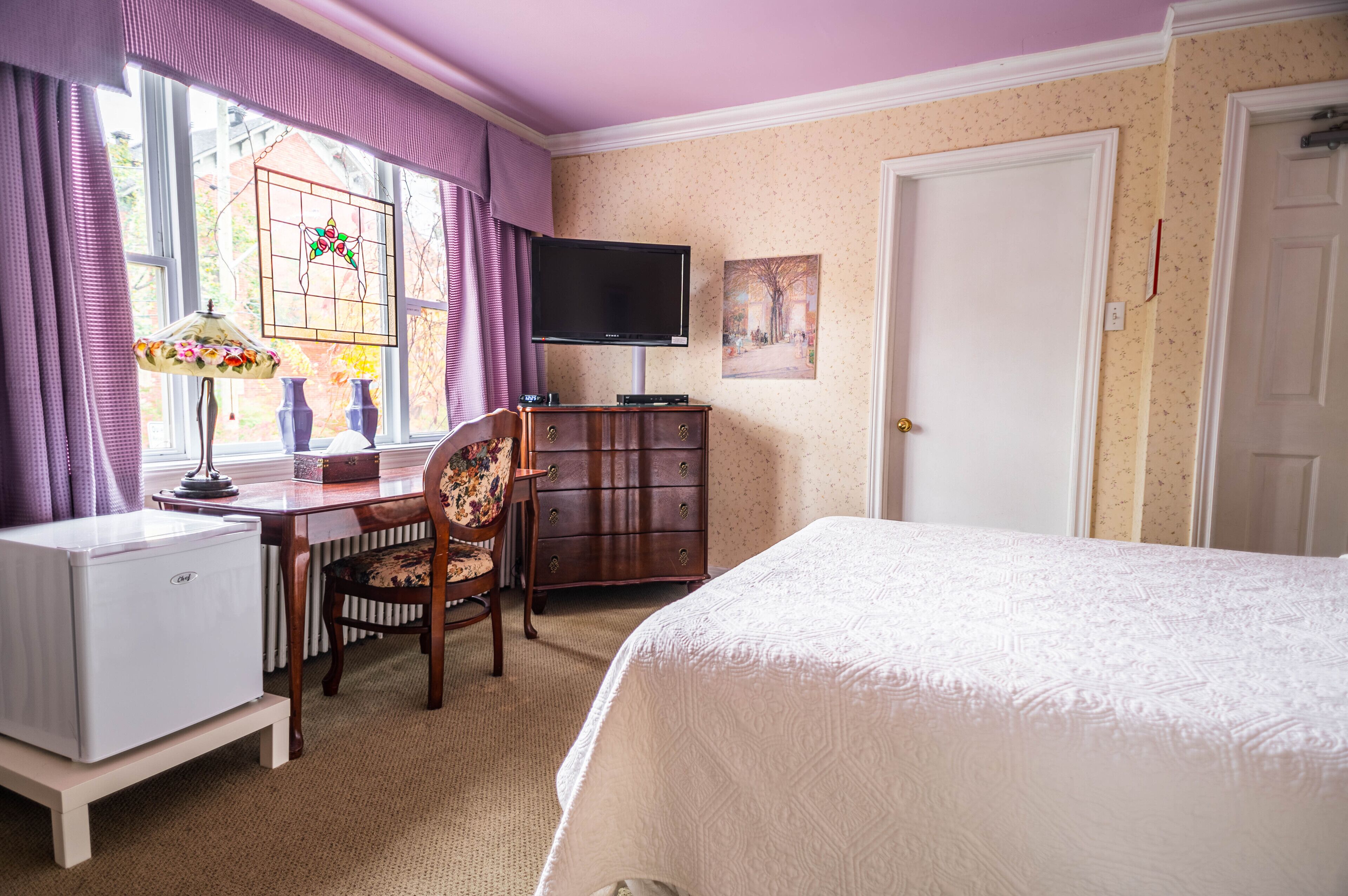 A bedroom with a bed, a desk with a computer, a chair, a dresser, and a television.