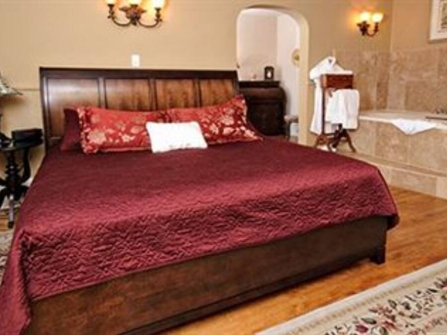 Quarto com cama grande, mesa de cabeceira, abajur e banheiro visível por um arco.
