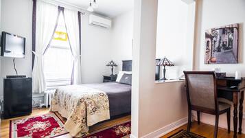 A bedroom with a bed, a desk, a chair, a TV, and a radiator.