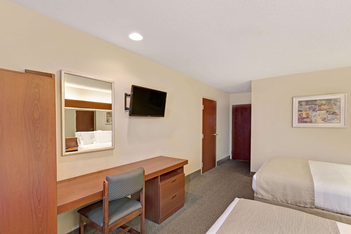 Une chambre d’hôtel avec un bureau en bois, une chaise, un lit, un téléviseur fixé au mur et une porte.