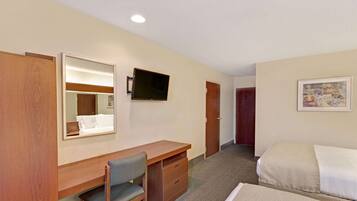 A hotel room with a wooden desk, a chair, a bed, a television mounted on the wall, and a door.