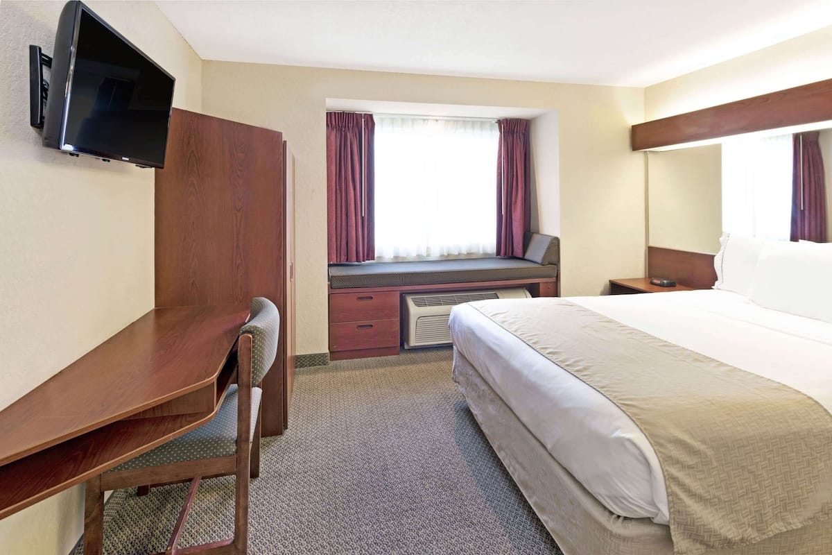 Une chambre d’hôtel comprenant un lit, un bureau, une chaise, un téléviseur fixé au mur et une fenêtre avec des rideaux.