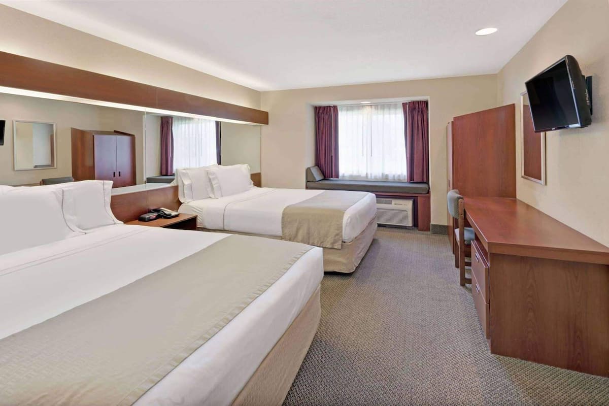 Une chambre d’hôtel avec deux lits, un bureau, une chaise, une télévision, une fenêtre avec des rideaux et un miroir.