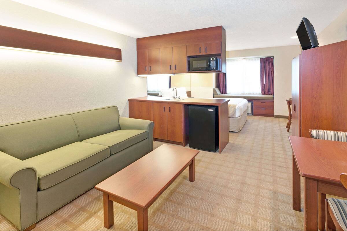 Une chambre d’hôtel compacte comprenant un coin cuisine, un canapé, une petite table à manger et un lit.