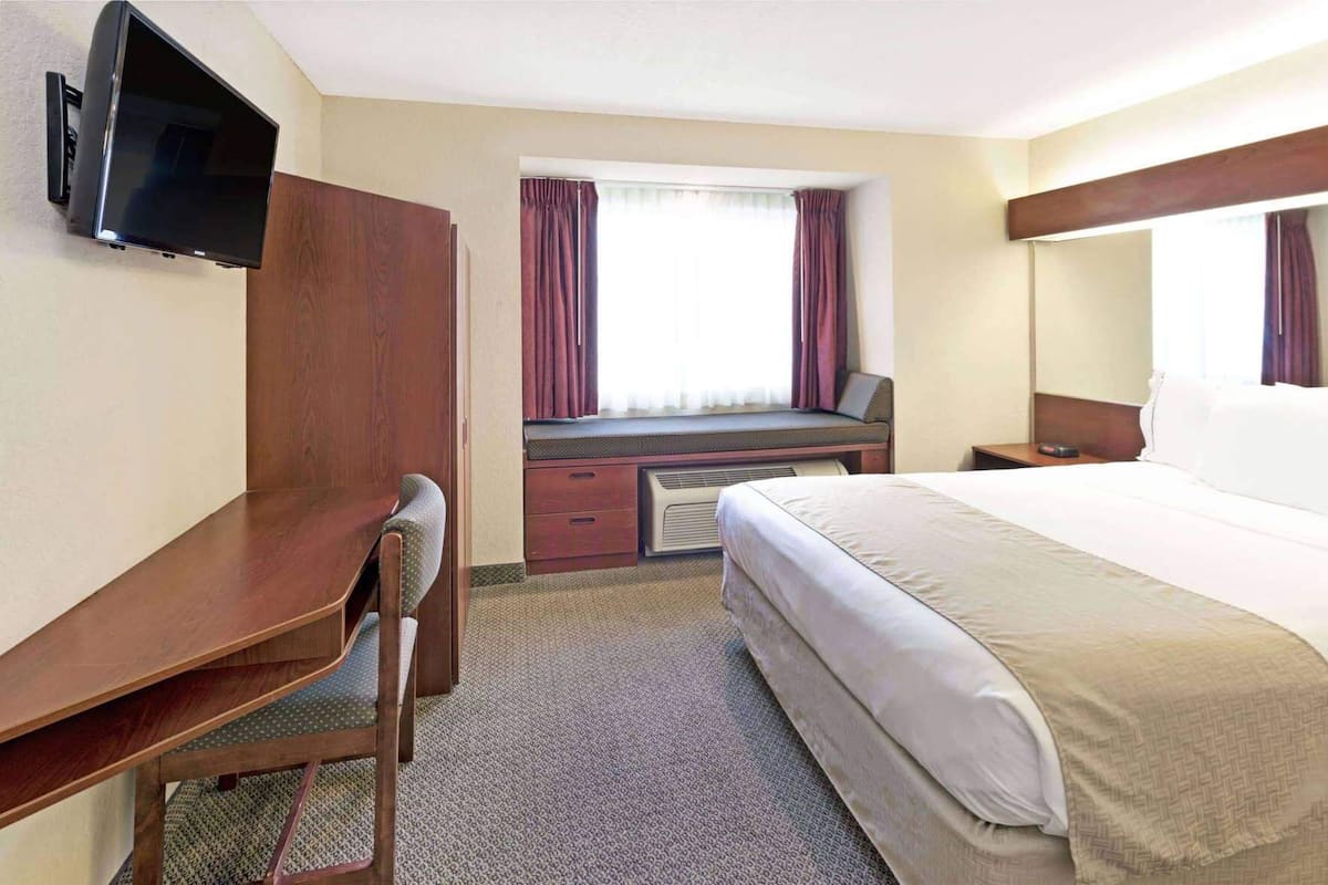 Une chambre d’hôtel équipée d’un lit, d’un bureau, d’une chaise, d’une télévision et d’une fenêtre avec des rideaux.