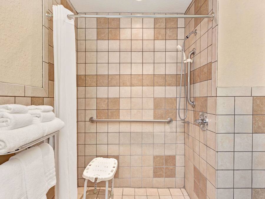 A shower area with a grab bar, a white towel rack, and a small stool.