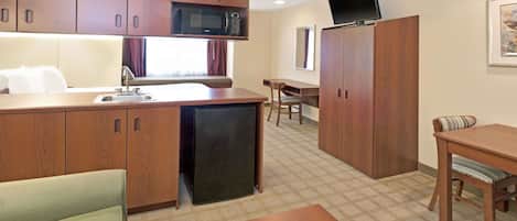Une chambre d’hôtel compacte comprenant un coin cuisine, un espace repas, un petit canapé et un téléviseur fixé au mur.