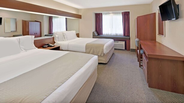 A hotel room with two beds, a desk, a chair, a TV, and a window with curtains.