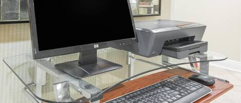 Una computadora con monitor, teclado e impresora sobre un escritorio de vidrio.
