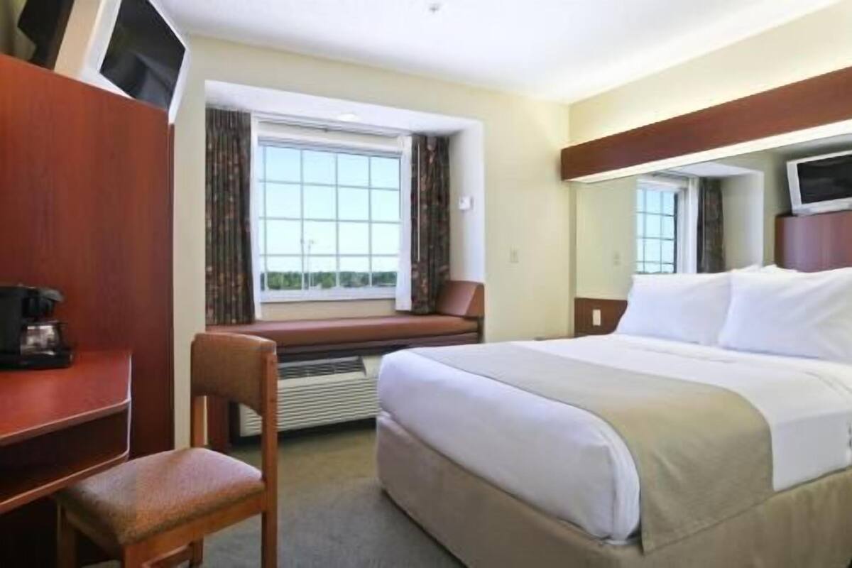 Habitación de hotel con cama, escritorio, silla, ventana y televisión.
