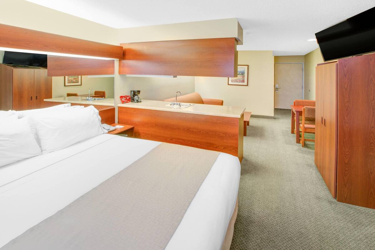Una habitación de hotel con una cama grande, un escritorio de madera, una silla, un televisor y un armario.