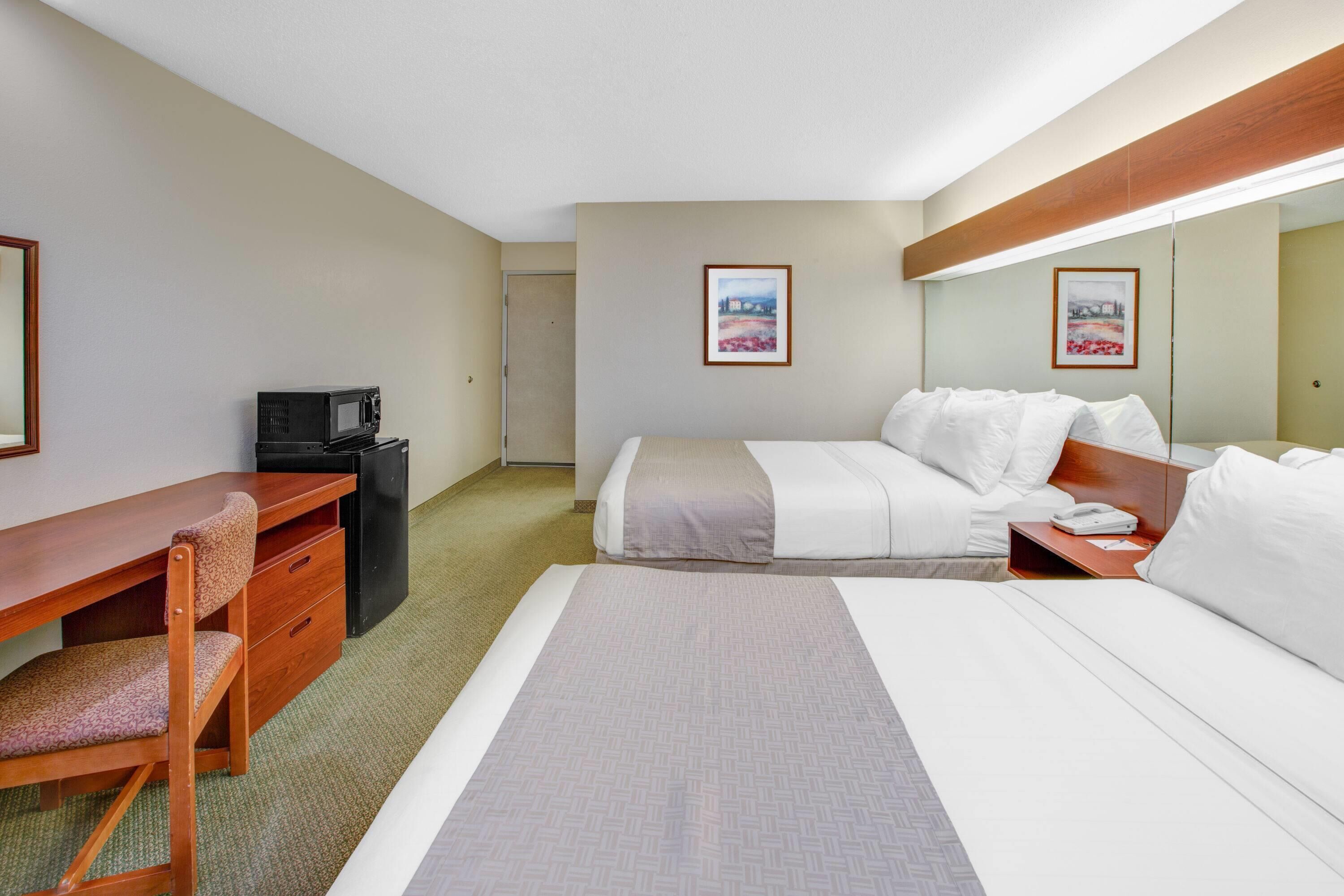 A hotel room with a bed, a desk, a chair, a microwave, and a small trash bin.