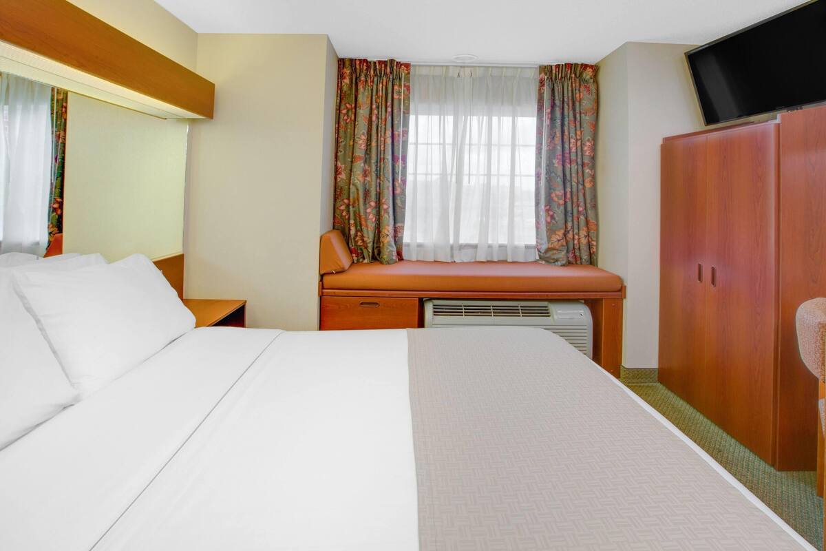 Una habitación de hotel con cama, escritorio, armario y televisor.