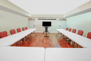 Conference room with a long table and rows of chairs, featuring a flat-screen television at the front.