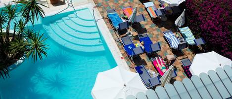 Un área de piscina con sillones de descanso, sombrillas y una terraza de baldosas.