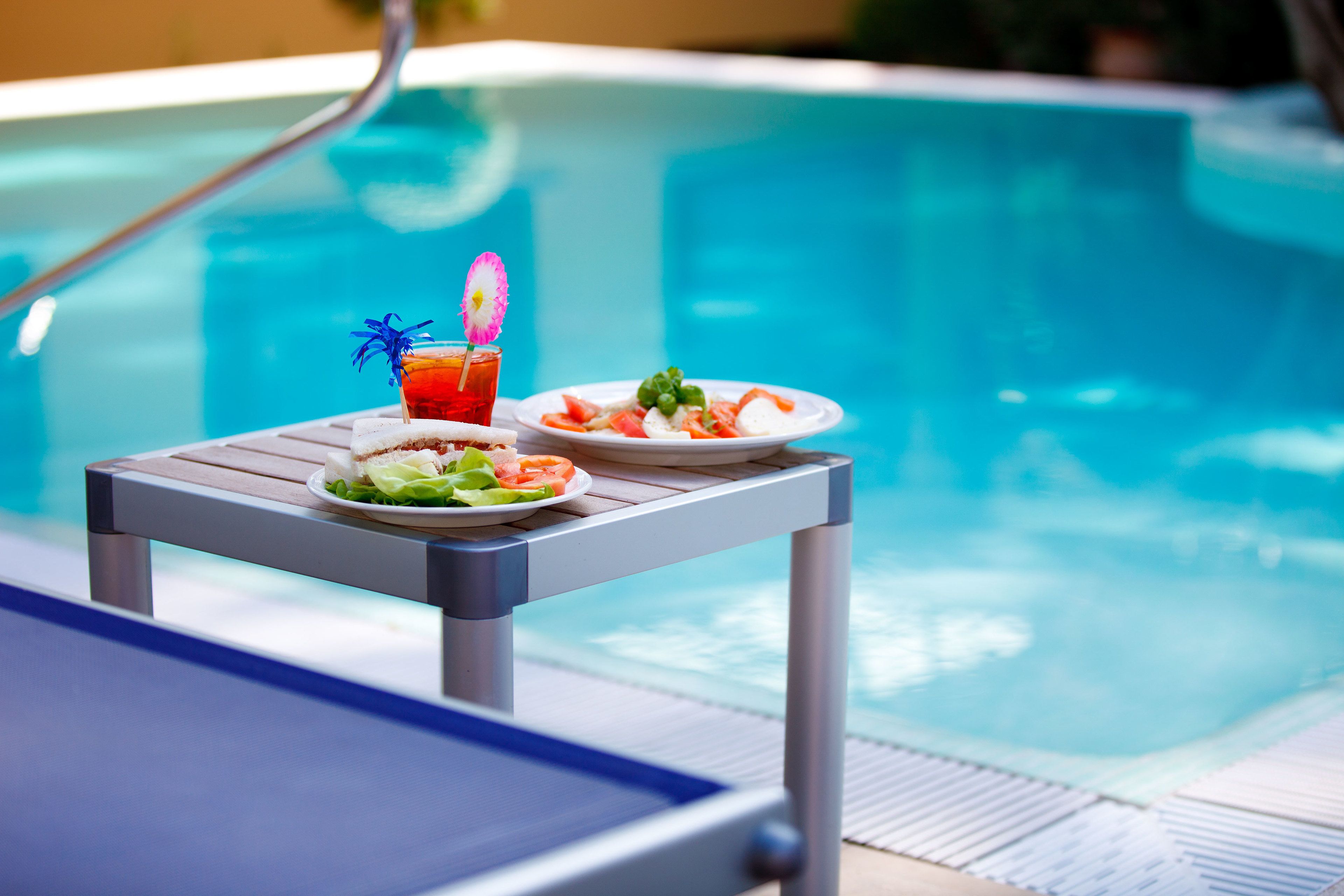 A poolside table with a plate of food and a drink.