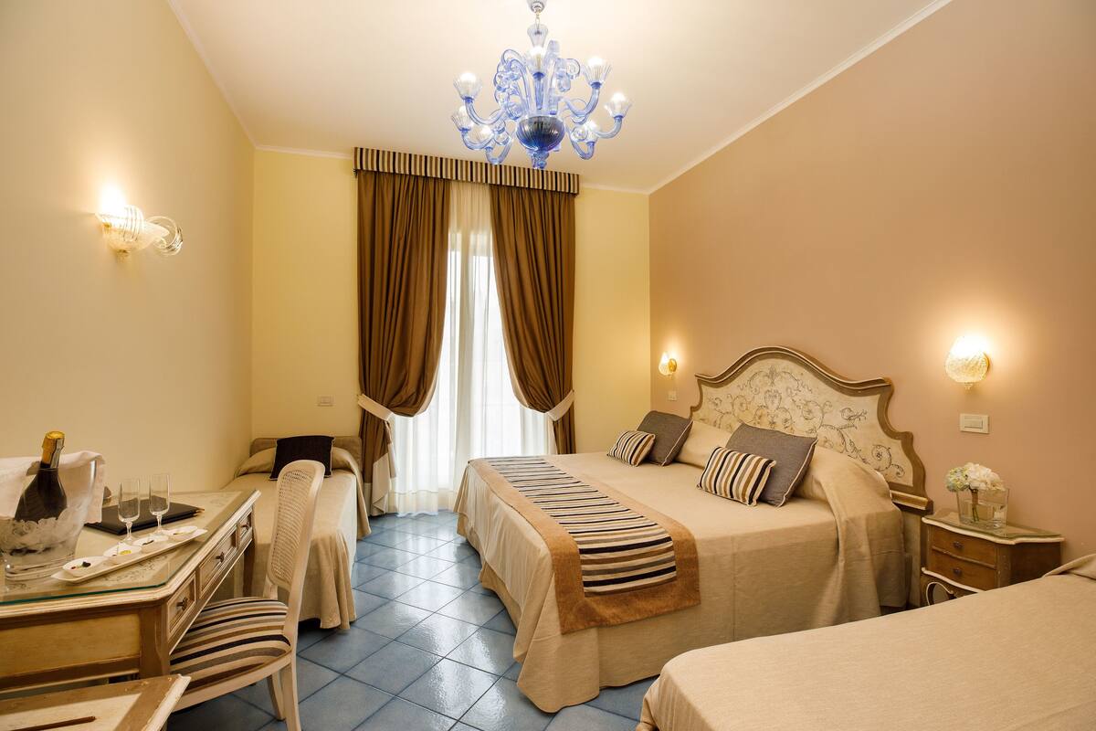 Habitación de hotel con dos camas, un escritorio, una silla, una araña y una mesita de noche con un florero.