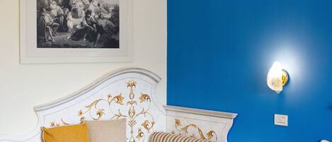A bedroom with a white bed, a blue accent wall, a framed black and white photo, and a decorative wall sconce.
