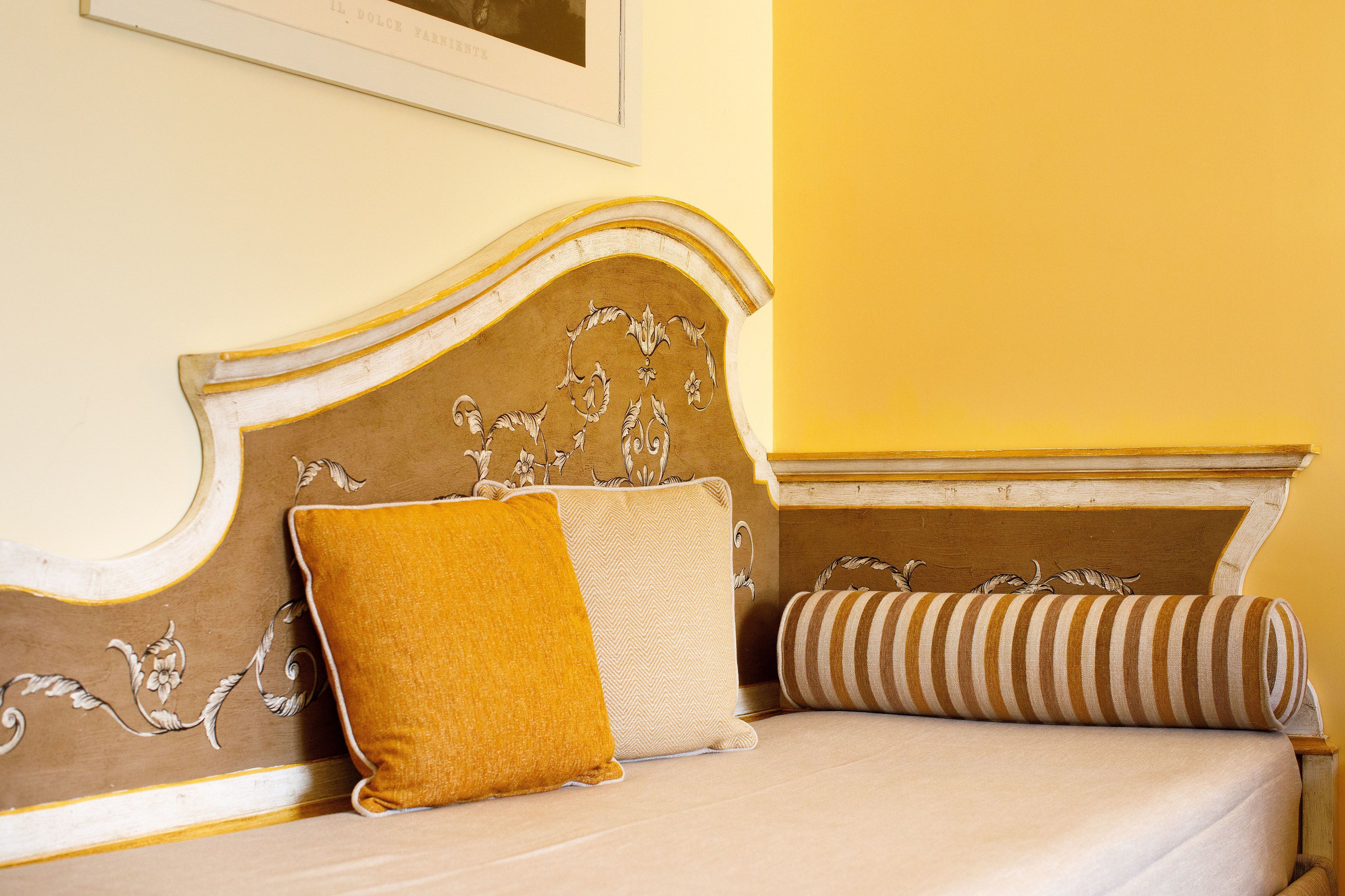 Un lit doté d’une tête de lit ornée de sculptures complexes, d’un coussin de couleur moutarde et d’un coussin à rayures.