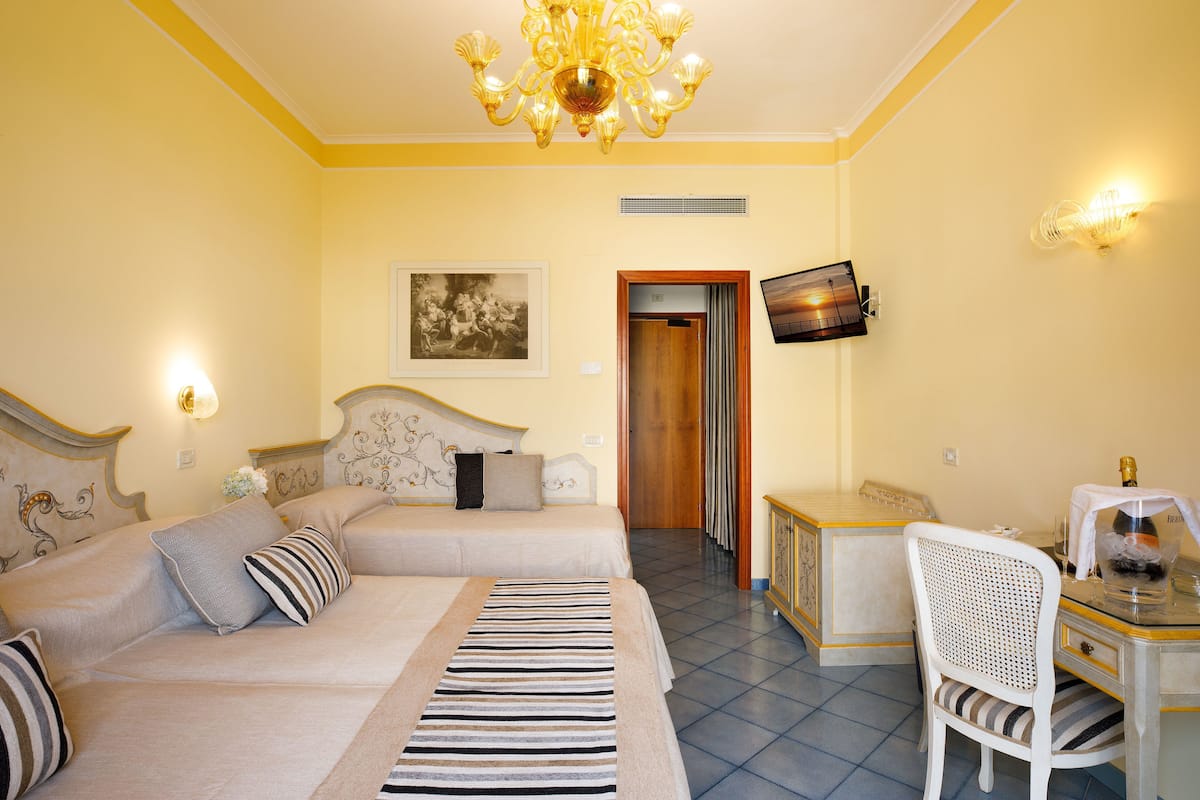 Una habitación de hotel con cama, un escritorio con silla, televisión y una araña.
