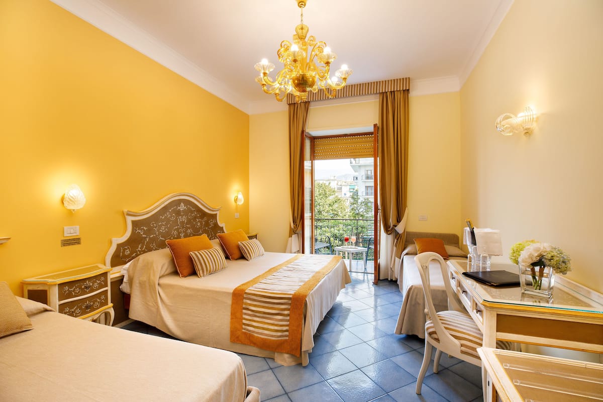 Habitación de hotel con una cama grande, un escritorio con una silla, una araña y vistas al exterior.