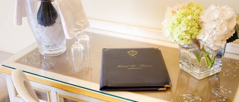 A glass table with a bottle of champagne, a glass, a black booklet, and a vase with flowers.