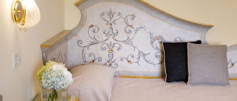 Una cama bien hecha con un cabecero decorativo, una mesita de noche con superficie de vidrio y un florero con flores.