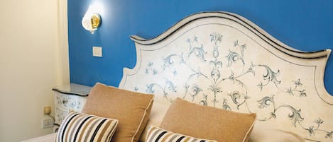 Ein Bett mit einem Kopfteil mit floralem Muster, zwei gestreifte Kissen und einem Nachttisch mit einer Lampe.