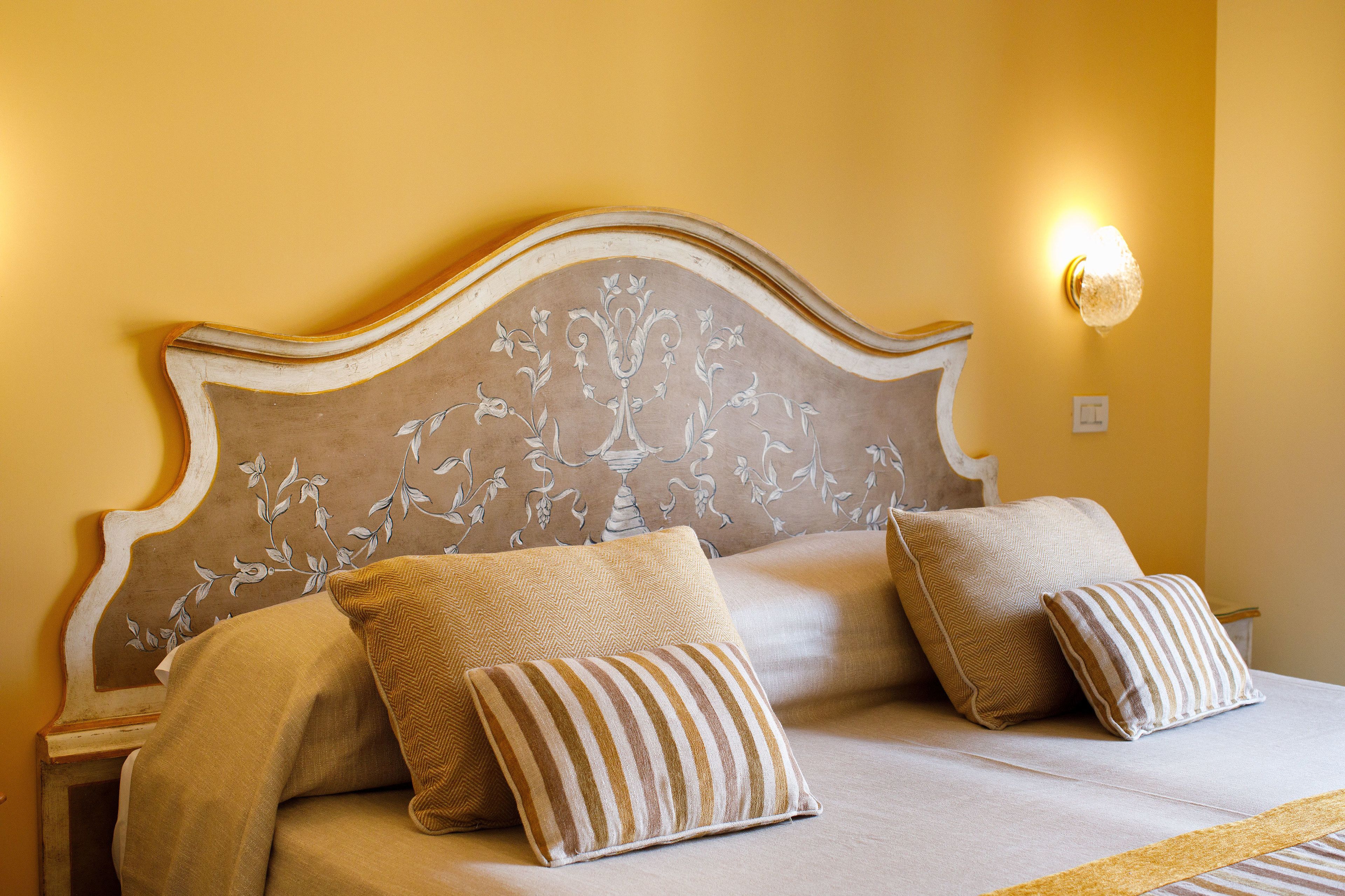Una cama con cabecera estampada con motivos florales, dos almohadas y una lámpara de noche.