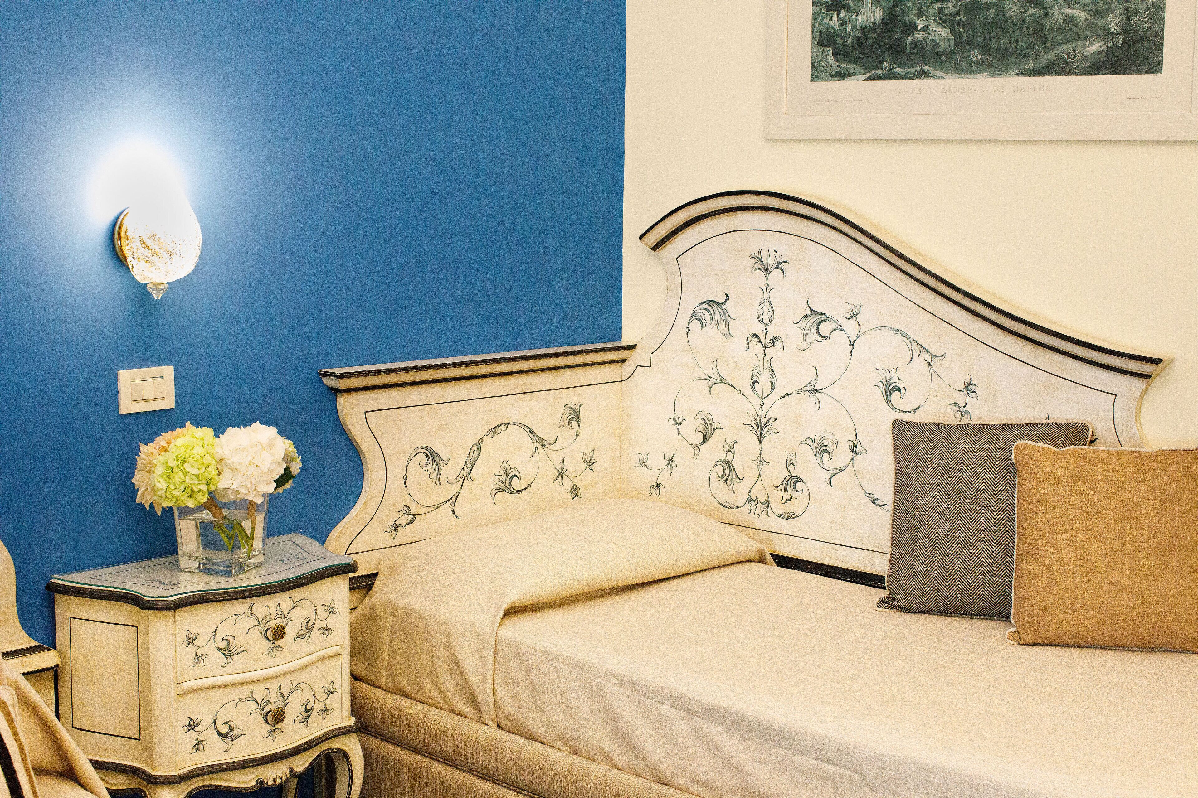 Une chambre à coucher avec un lit, une table de chevet, un vase de fleurs et un tableau encadré au mur.