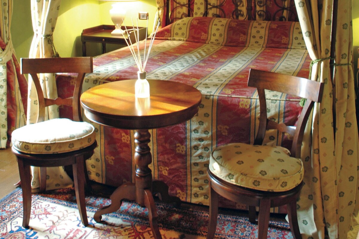 A cozy room with a bed, two chairs, a table, and a lamp.