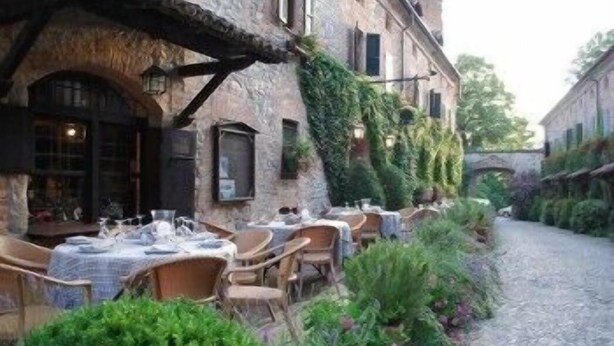An outdoor café with tables and chairs, a cobblestone path, and a building with a stone facade. - Hotel Residenza Torre di San Martino (Gazzola)
