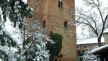 Una torre in mattoni con una bandiera, circondata da alberi e cespugli imbiancati dalla neve.