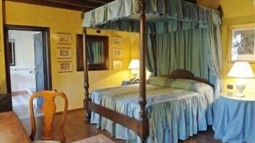 Una cama con dosel y cuatro columnas, una silla de madera y una mesita de noche con una lámpara.