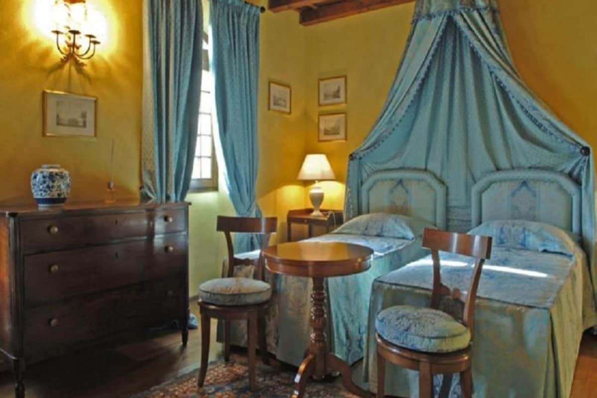 A bedroom with a four-poster bed, a wooden dresser, a round table, and two chairs.