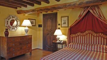 Une chambre à coucher avec une commode en bois, deux lampes de chevet, un lit à baldaquin rouge et une porte en bois.